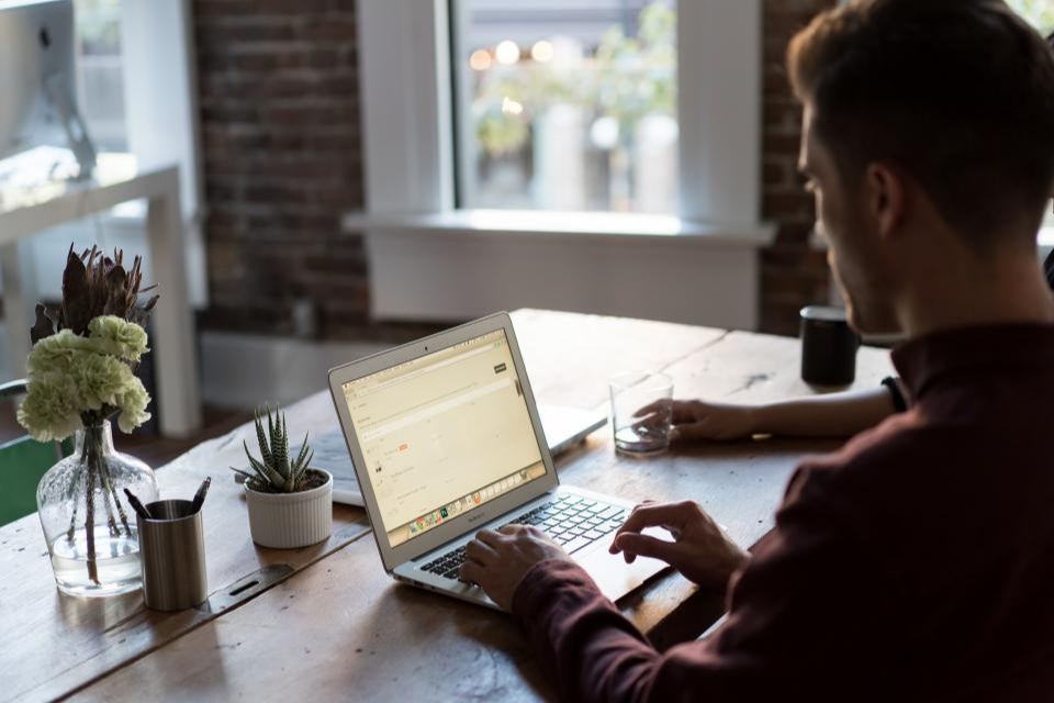 Man die typt op een laptop aan een tafel bij het raam